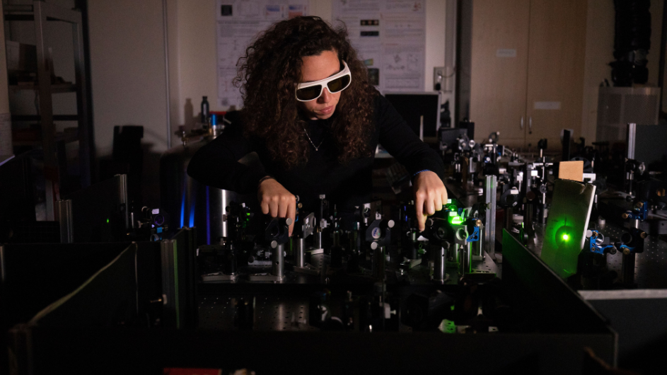 Chiara, wearing protective glasses, adjusts components to a green laser. 