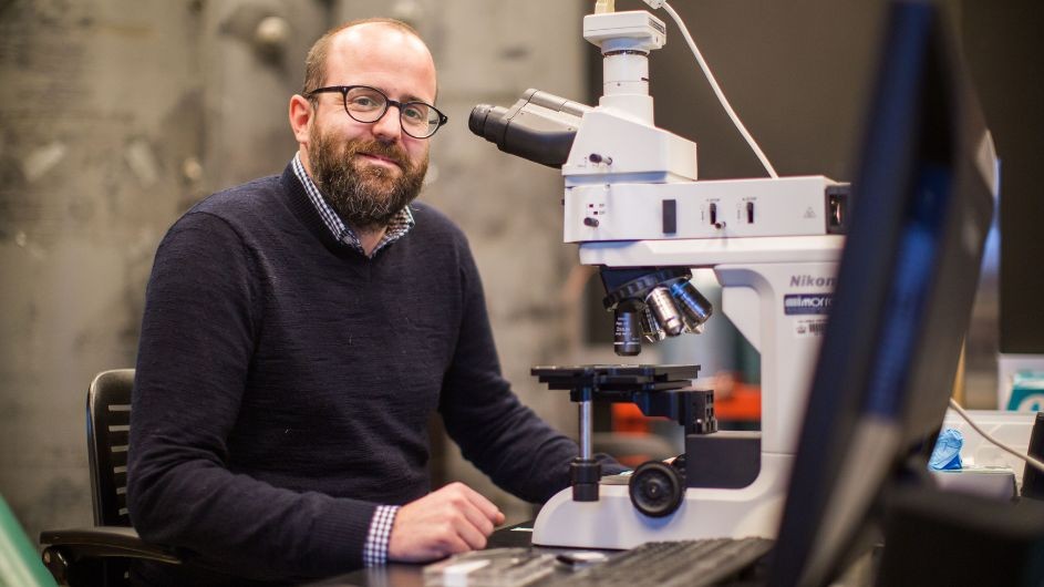 Cory Dean, Columbia University Physics Cory sitting in front of a microscope