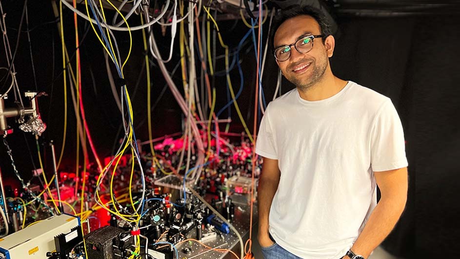 Debayan Mitra, a Columbia University postdoctoral fellow working with physicist Tanya Zelevinsky, poses in front of an optical table. 