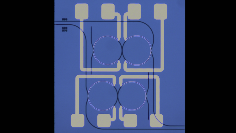 Microscope Image of SiN coupled-ring device. The mode interaction position is thermally tuned via integrated heaters to turn on and off the degenerate parametric oscillator for random number generation. Microscope Image of SiN coupled-ring device. The mode interaction position is thermally tuned via integrated heaters to turn on and off the degenerate parametric oscillator for random number generation.